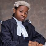 Kindness Idahosa Esq., posing with her wig and barrister attire, sitting on a wheelchair in a portrait photo.