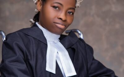 Kindness Idahosa Esq., posing with her wig and barrister attire, sitting on a wheelchair in a portrait photo.