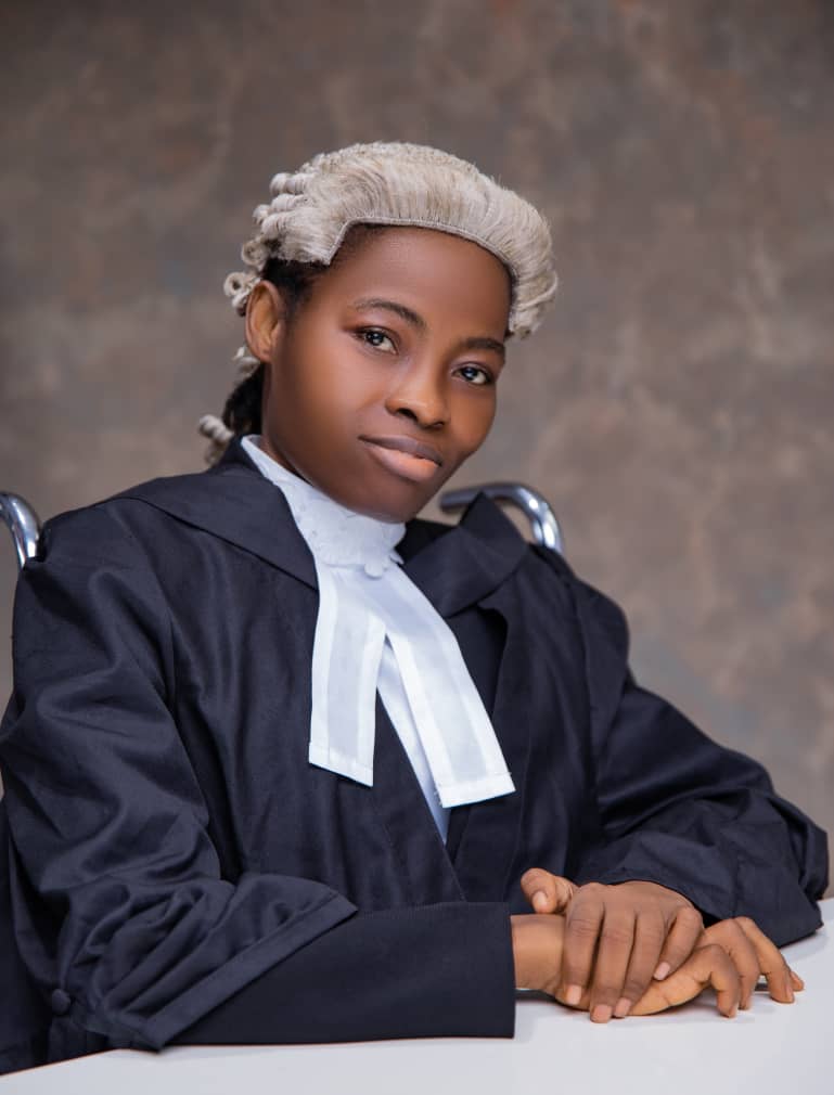Kindness Idahosa Esq., posing with her wig and barrister attire, sitting on a wheelchair in a portrait photo.