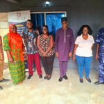 NAPVID staff and SONKE representatives pose for a group photograph outside the organisation’s secretariat in Benin City, Edo State, in front of a NAPVID banner.